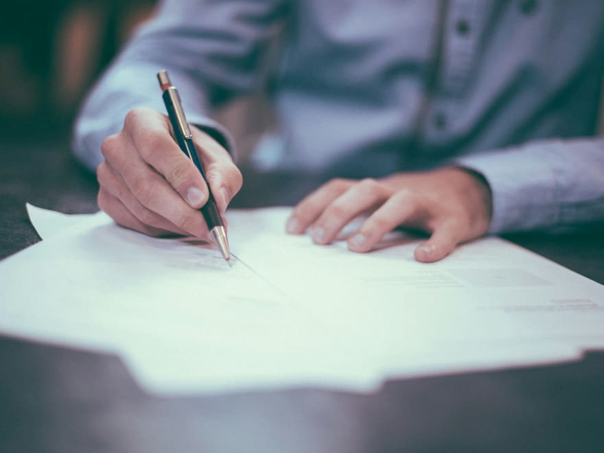 Mãos assinando um documento sobre uma mesa de trabalho.